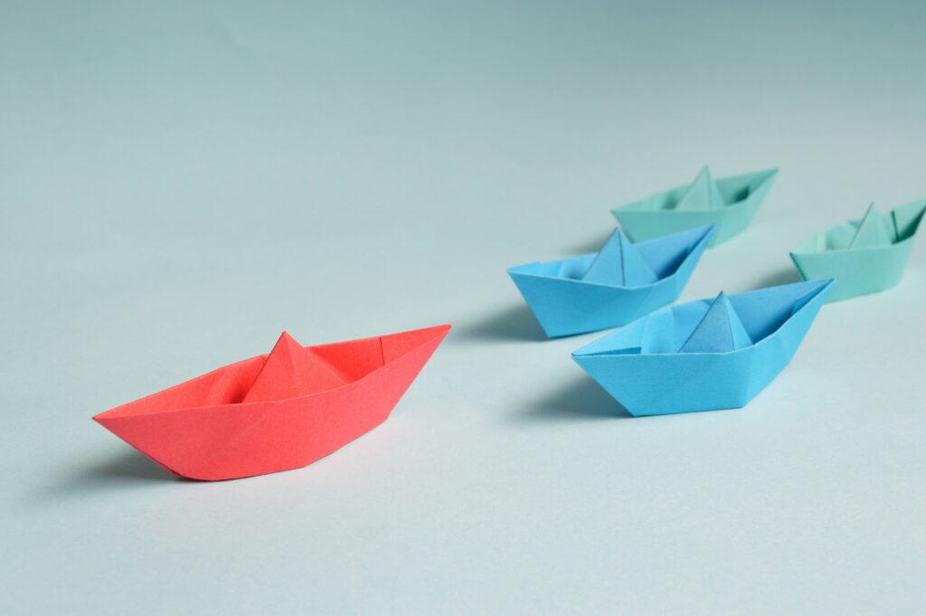 A group of paper boats with a red paper boat leading the others